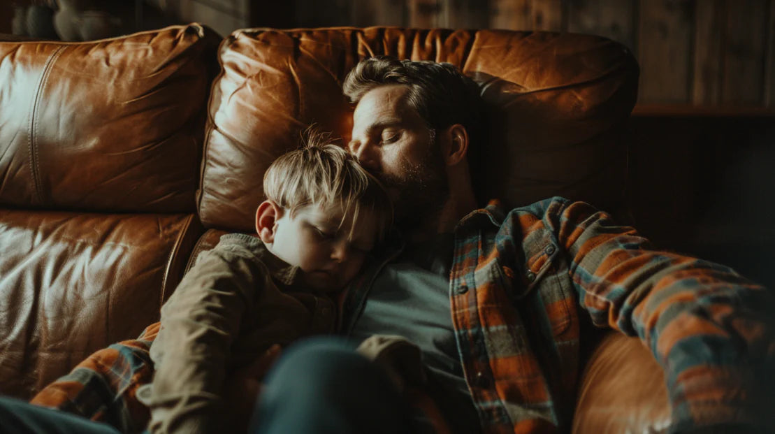A father and his son asleep on a leather couch
